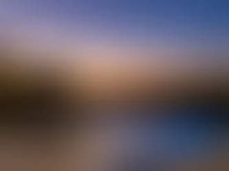 Blurry landscape at sunset with blue sky fading to orange on the horizon and dark foreground shapes
