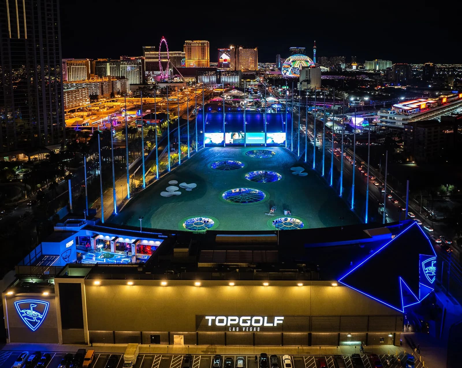 Aerial night view of Topgolf Las Vegas with blue-lit driving range and city skyline