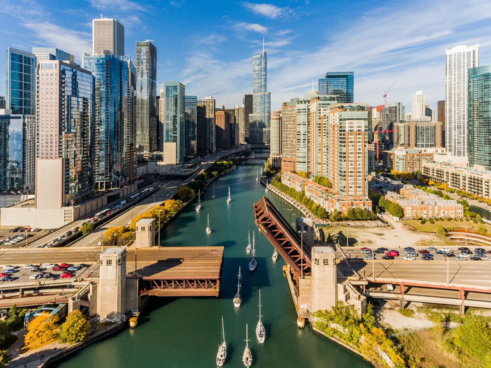 Aerial view of a city skyline with a waterway, sailboats, and glass-clad skyscrapers lining both sides
