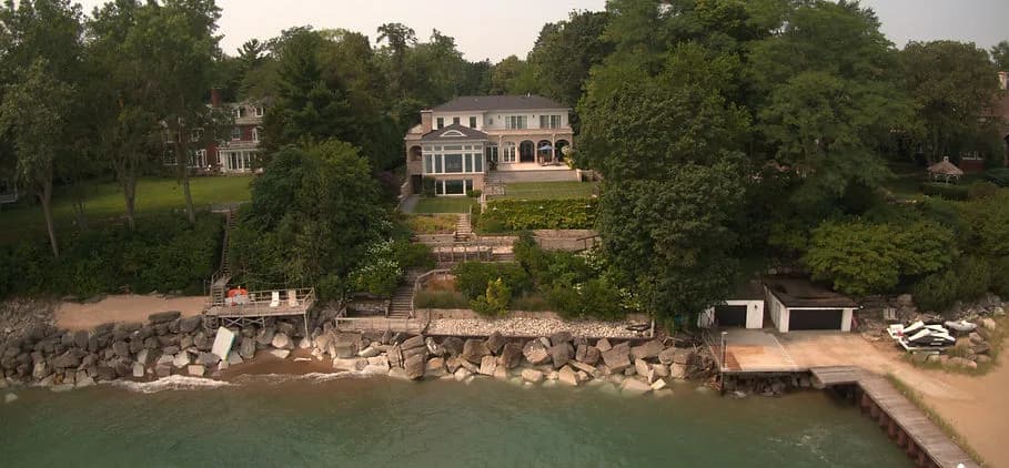 Waterfront estate with a large house, terraced gardens, rocky shoreline, and a wooden dock