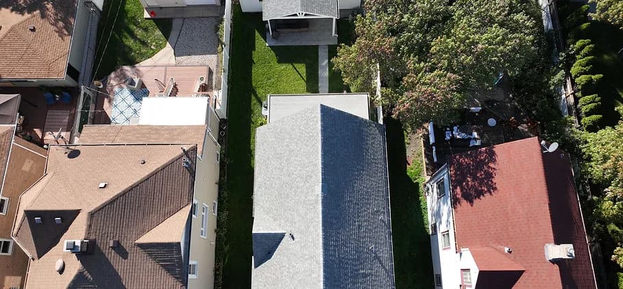 Aerial view of several residential rooftops, small backyards, and trees between houses
