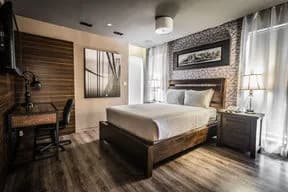 Bedroom with wooden bed, two nightstands with lamps, desk and chair, wall art, and windows