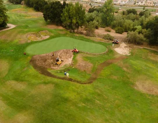 Aerial view of a circular green area under construction with excavators on a grassy site