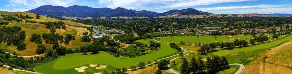 Panoramic view of a winding golf course with greens, sand bunkers, trees and hills and distant mountains