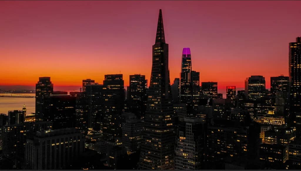 City skyline at sunset with orange and purple sky and lit office windows