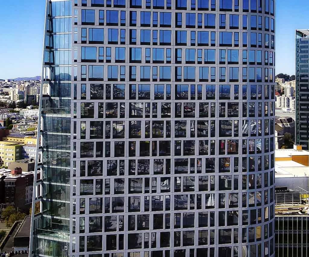 Curved glass office tower with a grid of square windows reflecting the city