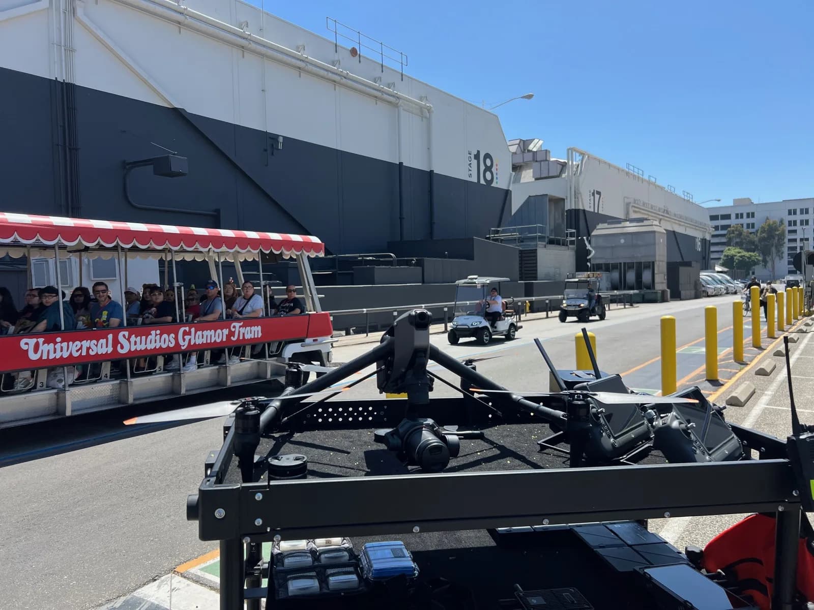 Universal Studios Glamour Tram with passengers under a red-and-white canopy; drone gear visible in foreground