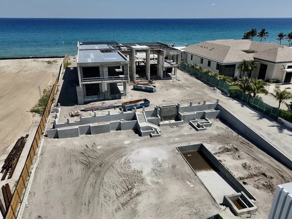 Aerial view of a beachside construction site with an unfinished concrete building and surrounding walls