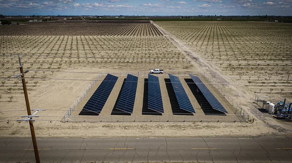 Drone shot of several rows of solar panels fenced in, with road in foreground and a white pickup nearby