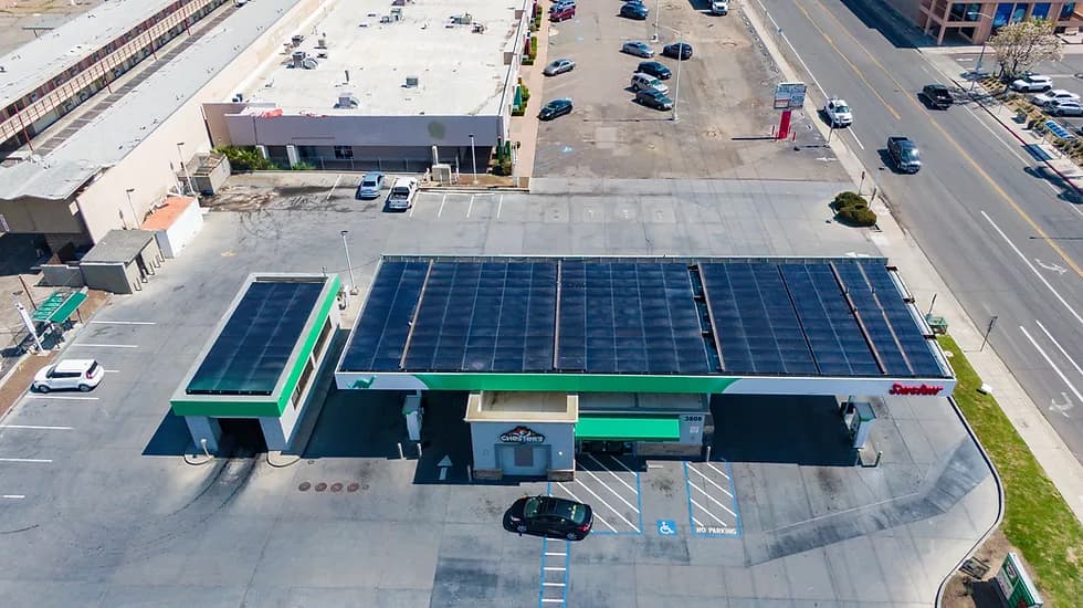 Aerial view of a building with a large solar panel roof and green trim, with a parking lot