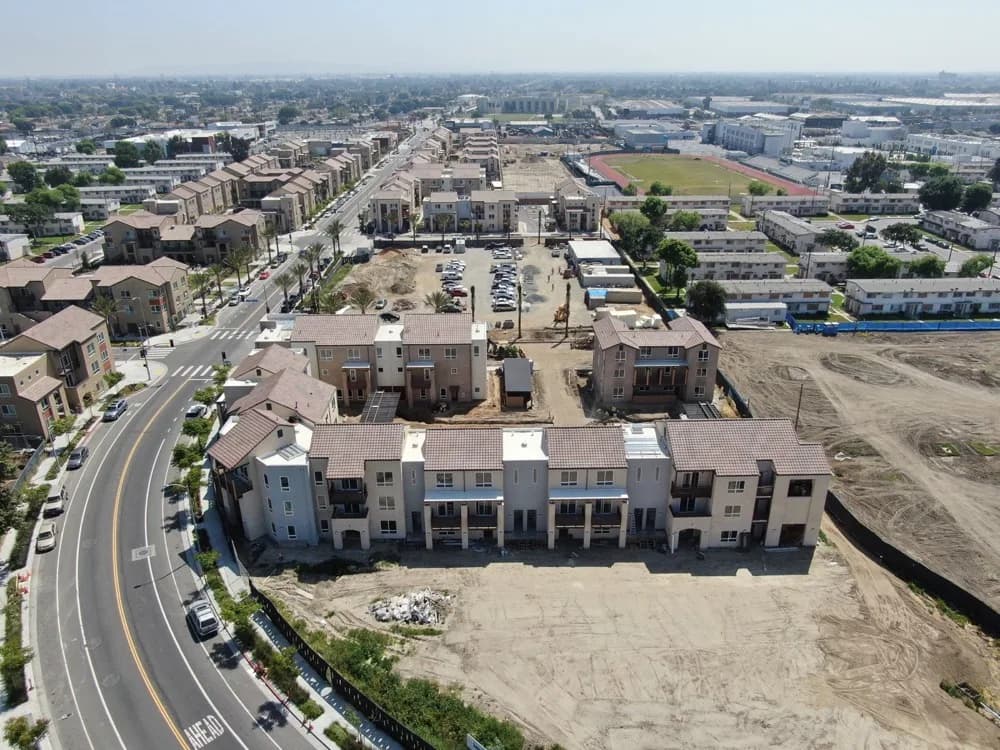 Aerial view of a residential development with row of townhouses along a curved road and a construction site