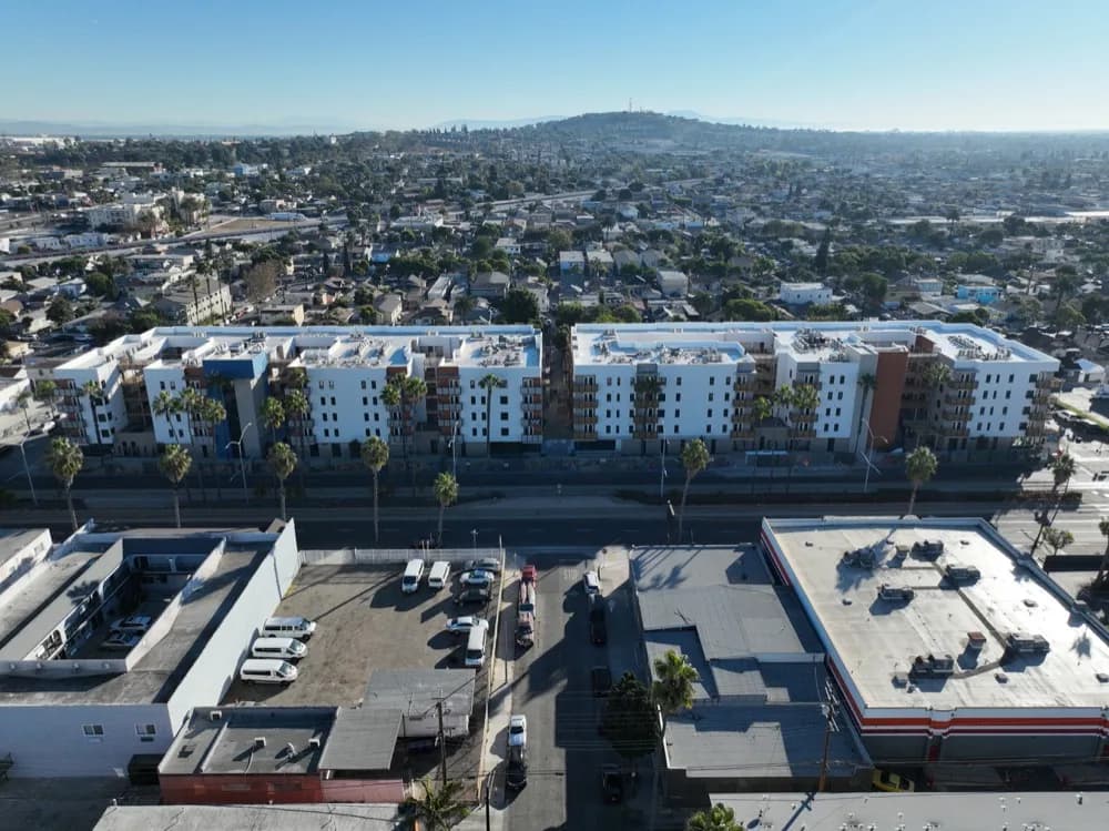 Aerial view of a residential block with white buildings along a street, palm trees, and a parking lot