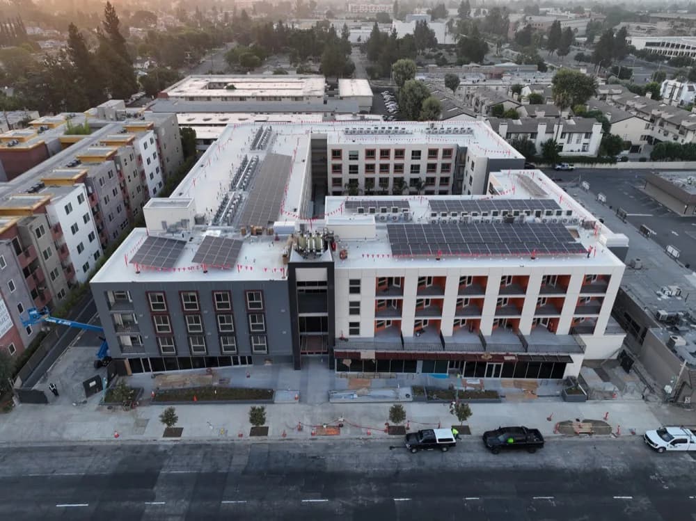 Aerial view of a U-shaped building under construction with solar panels on flat roofs and a crane nearby
