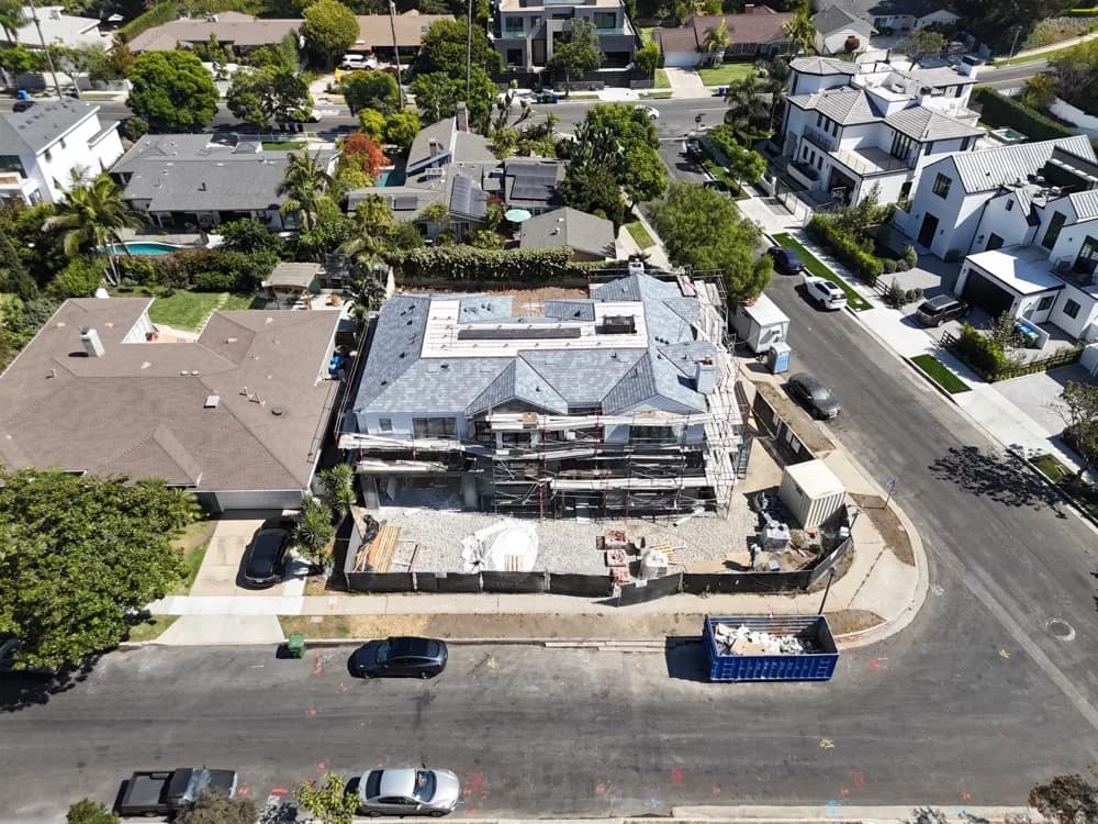 Aerial view of a two-story house under construction with scaffolding, surrounded by a neighborhood