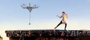 Drone hovers above a graffiti-covered ledge with a person standing on the edge, arms outstretched