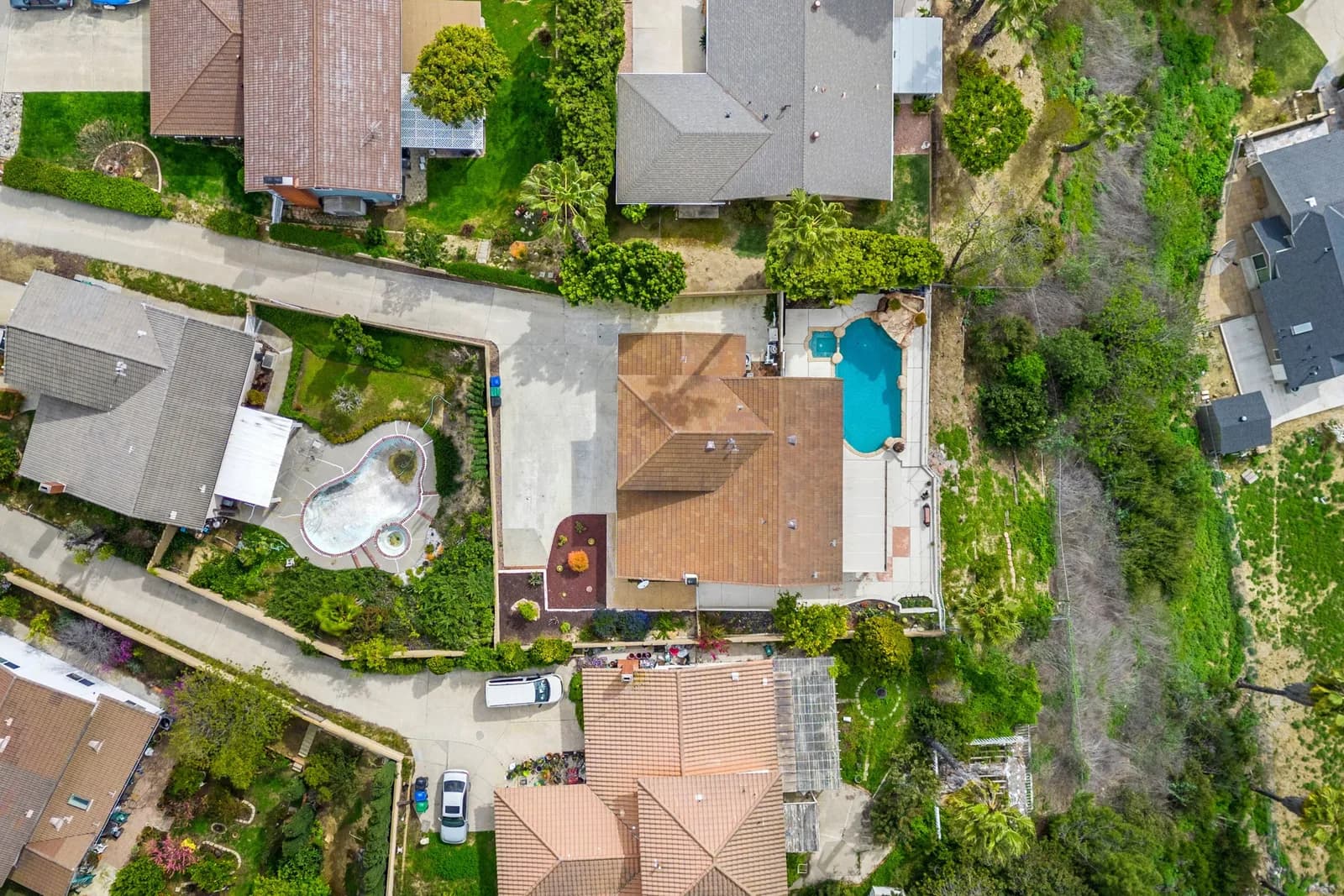Aerial view of a suburban neighborhood with tiled roofs, green lawns, and two pools visible in backyards