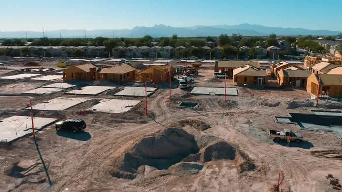 Wide aerial view of a residential construction site with dirt mounds, partially built houses, and trucks