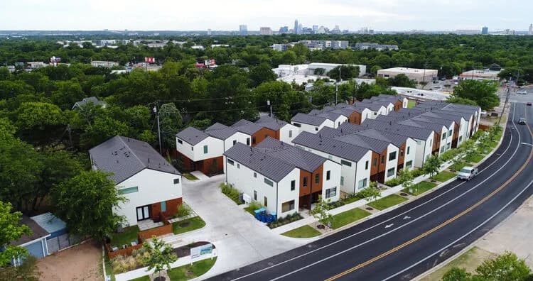 Row of modern townhouses along a curved street with trees and a distant city skyline