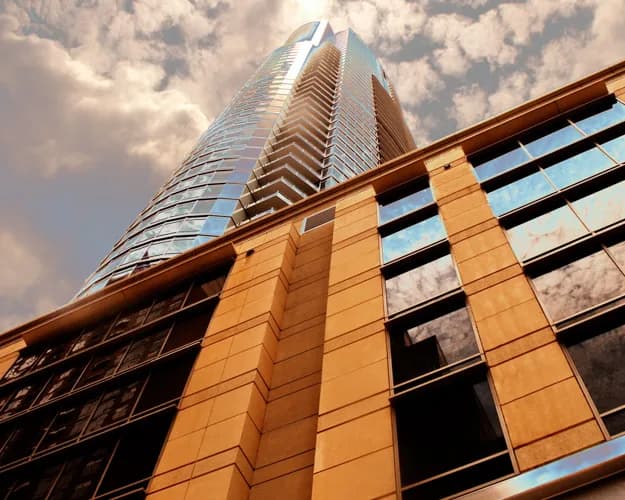 Low-angle view of a tall glass skyscraper with a tan stone facade and cloudy sky
