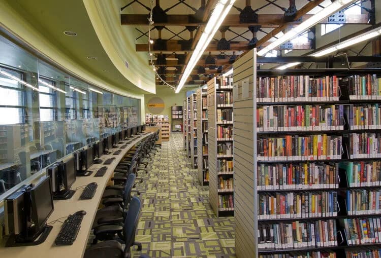 Library interior with computer workstations along a curved glass wall and tall bookshelves