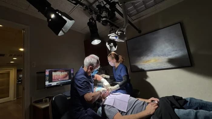 Dentists performing a dental procedure on a patient in a clinic, monitor displaying a dental image