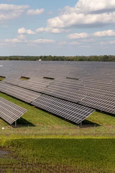Rows of solar panels on a grassy field with a low fence, under a partly cloudy sky