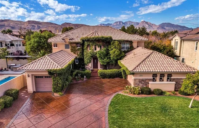 Aerial view of a tan two-story house with tile roof, ivy on walls, and a curved driveway