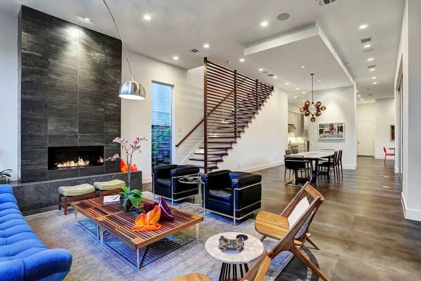 Open-plan living area with a stone fireplace, modern staircase, blue sofa, and dining table