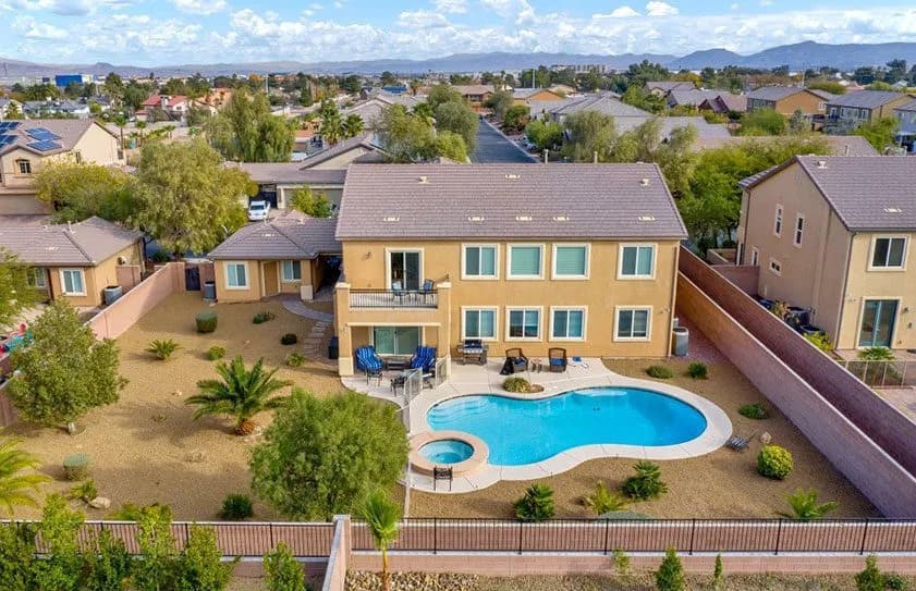 Aerial view of a beige two-story house with a kidney-shaped pool in a fenced backyard and desert landscaping
