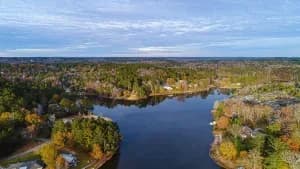 Aerial view of a winding waterway with tree-lined shores and houses under a blue cloudy sky