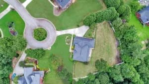 Aerial view of a suburban neighborhood with green lawns, trees and gray roofs around a roundabout