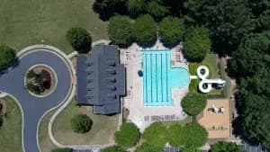 Aerial view of a large house with turquoise pool, white deck, dark roof, curved driveway, and trees