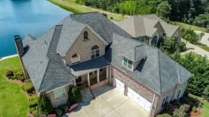 Aerial view of a large two-story house with gray roof, attached garage, front lawn, and a lake nearby