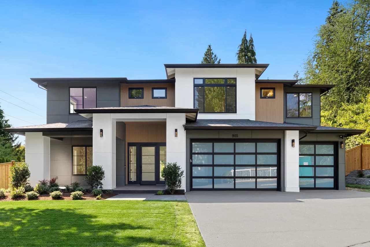 Modern two-story house with white, gray, and wood siding and large glass-panel garage doors