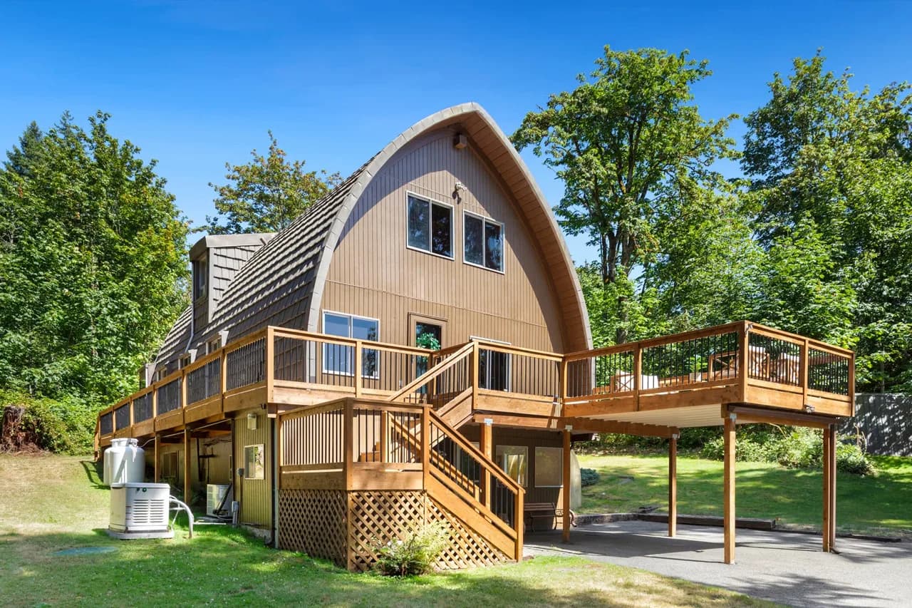 Wood-clad house with a tall arched roof, wraparound deck and exterior stairs