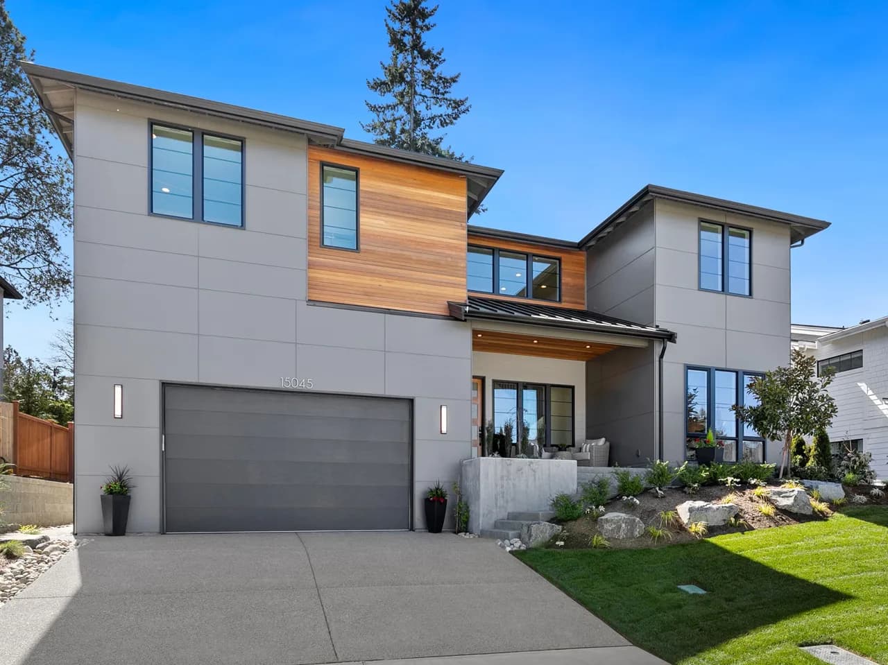 Modern two-story house with gray panels, wood accent, large windows, and a two-car garage