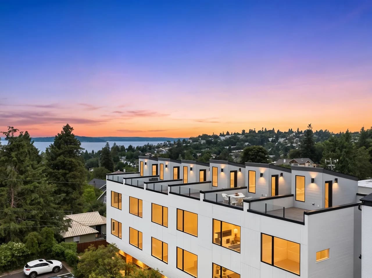 Modern white apartment building with rooftop terraces and glowing windows, hillside neighborhood at sunset