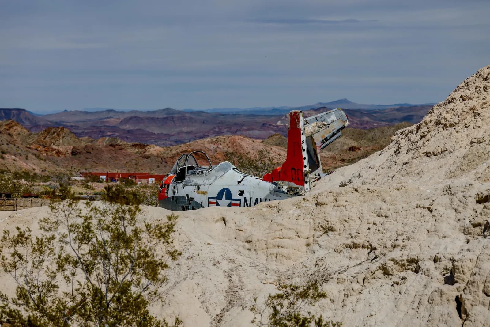 Desert landscape with a weathered military aircraft wreck, red tail, Navy markings, and distant mountains