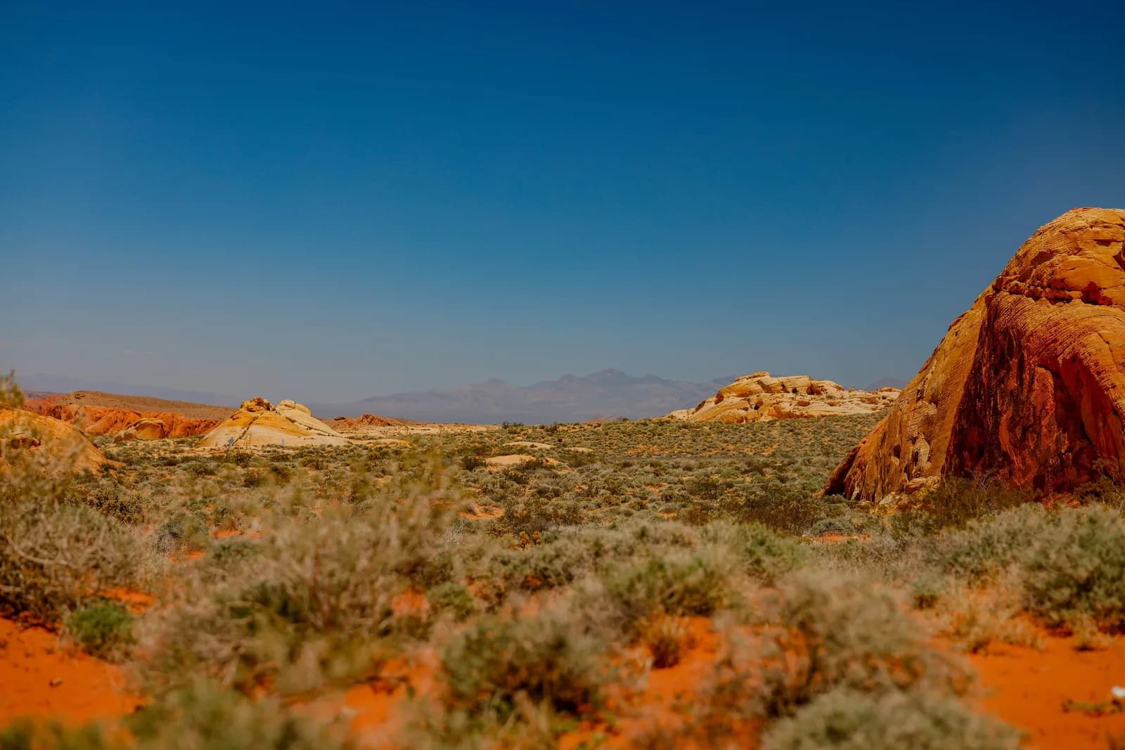 Desert landscape with a large orange rock formation on the right and a blue sky
