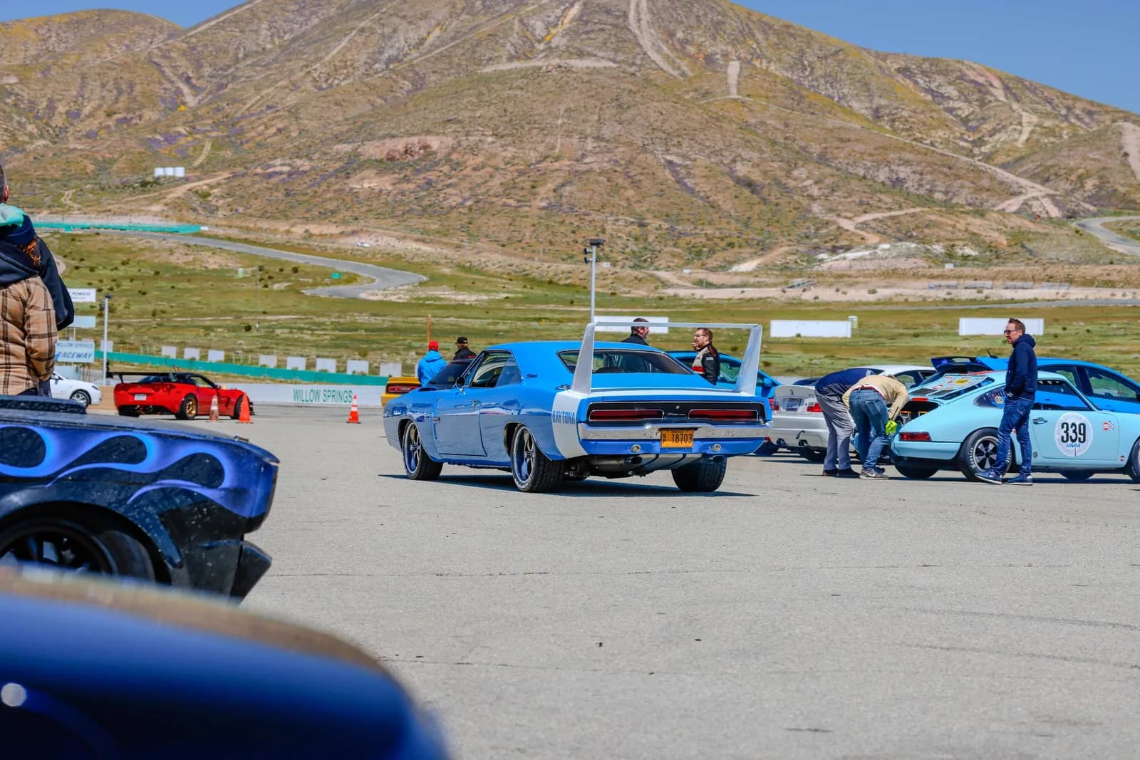 Blue vintage Dodge Charger with large rear wing at Willow Springs Raceway, with other cars and people