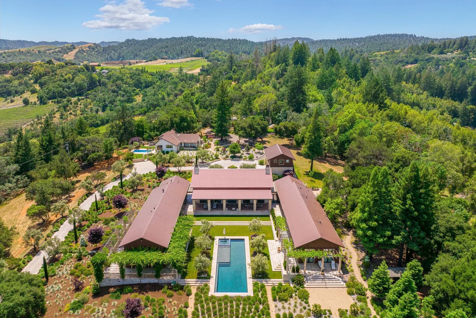 Aerial view of a large estate with red-roofed buildings, a rectangular pool, and manicured gardens