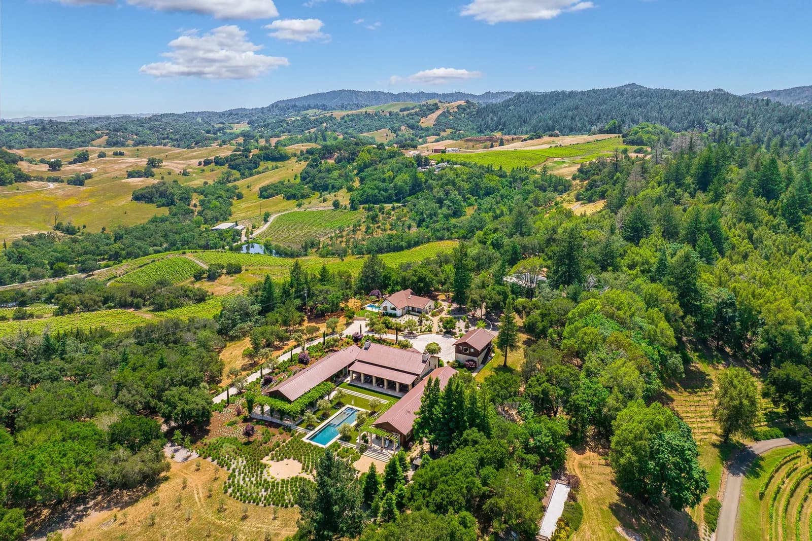 Aerial view of a large estate with red roofs, swimming pool, landscaped gardens, and surrounding farmland