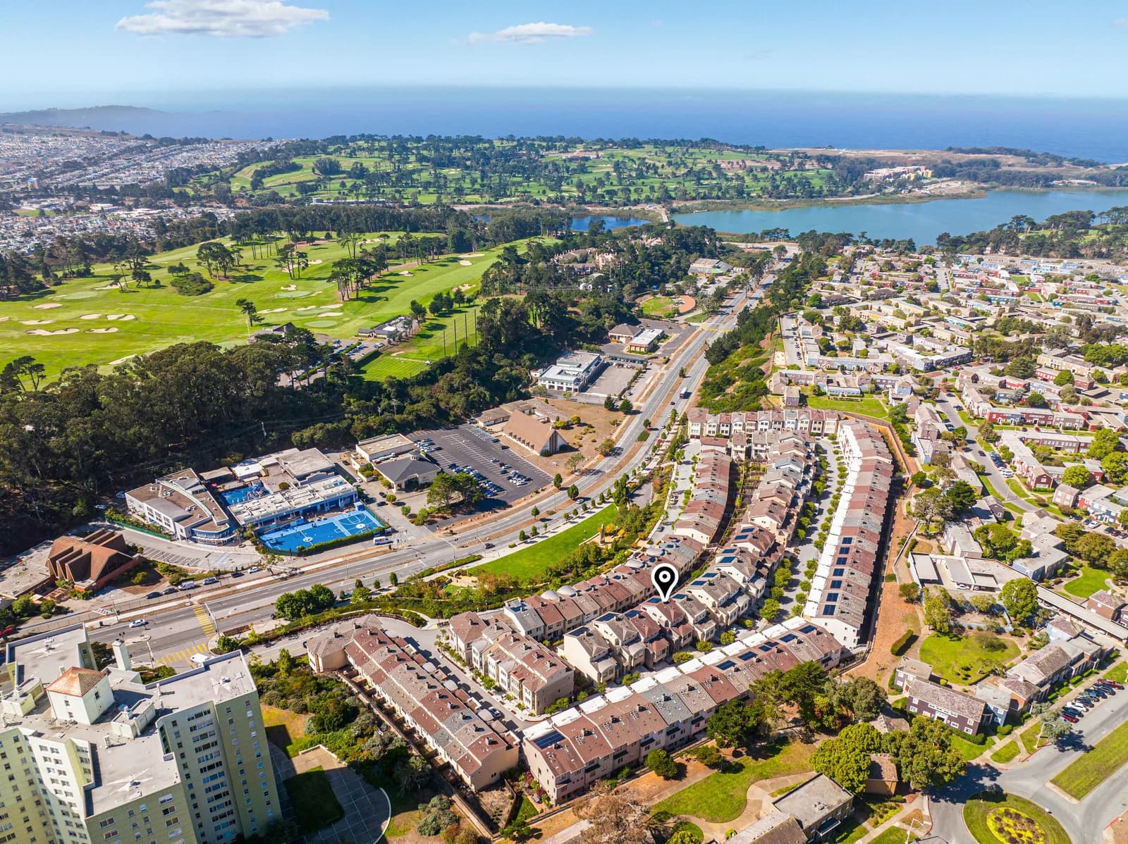 Aerial view of a coastal suburb with a golf course, ponds, and a row of townhouses marked by a pin