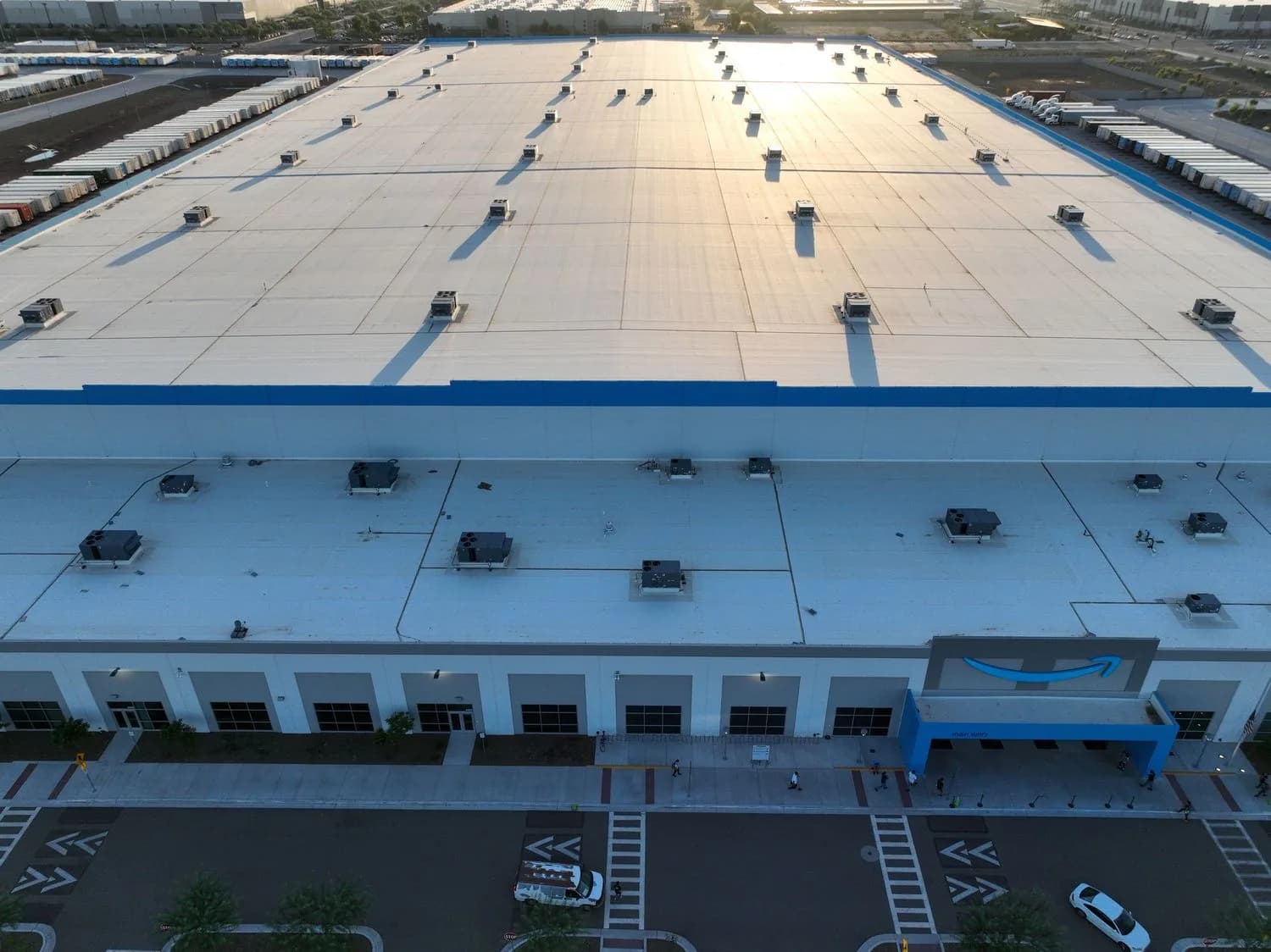 Warehouse rooftop with multiple HVAC units, long shadows, street and Amazon smile logo at entrance