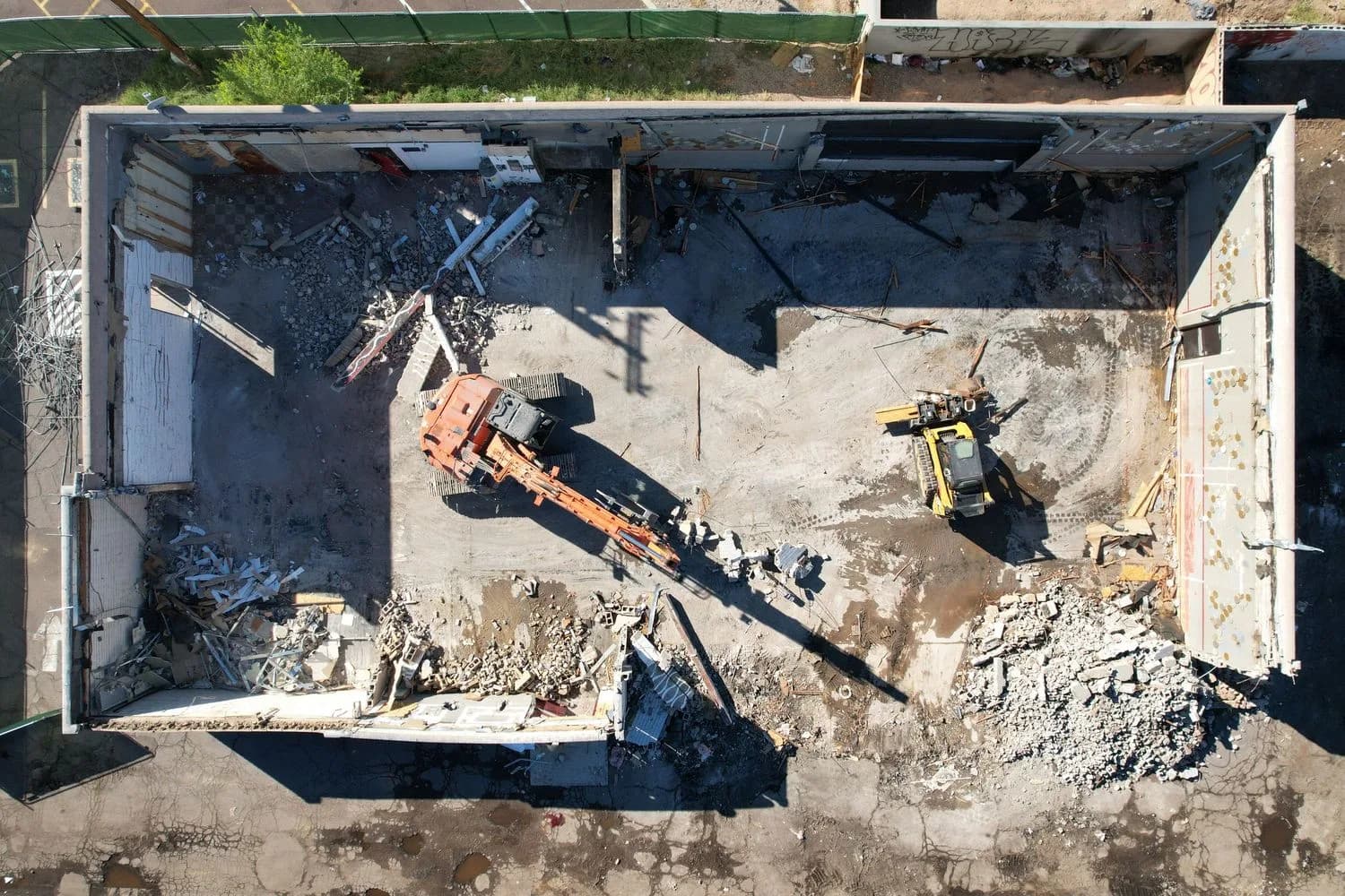 Top-down view of a demolition site inside a rectangular building with excavators and rubble