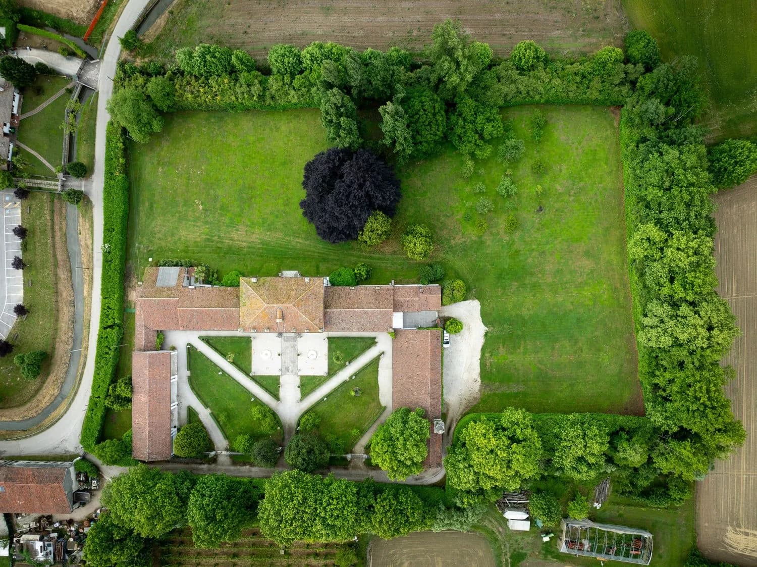 Aerial view of farmhouse complex with central courtyard, large grassy lawn and surrounding tree borders