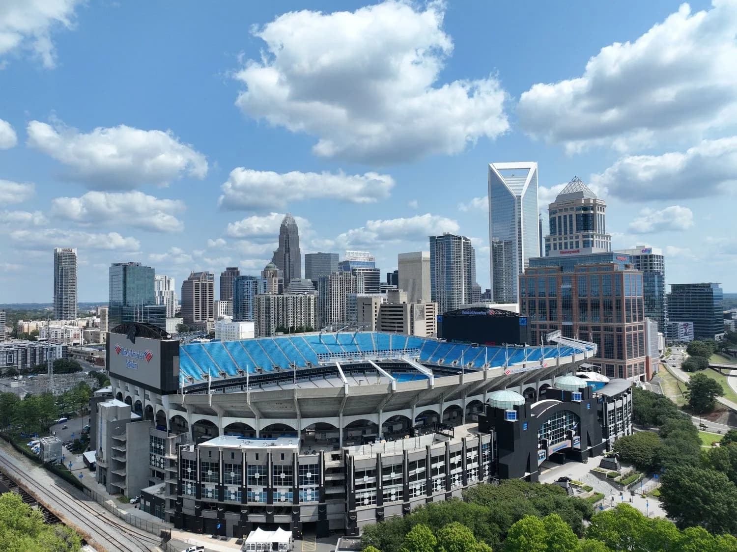 Aerial view of a large stadium with blue seats and surrounding city skyline under a partly cloudy sky