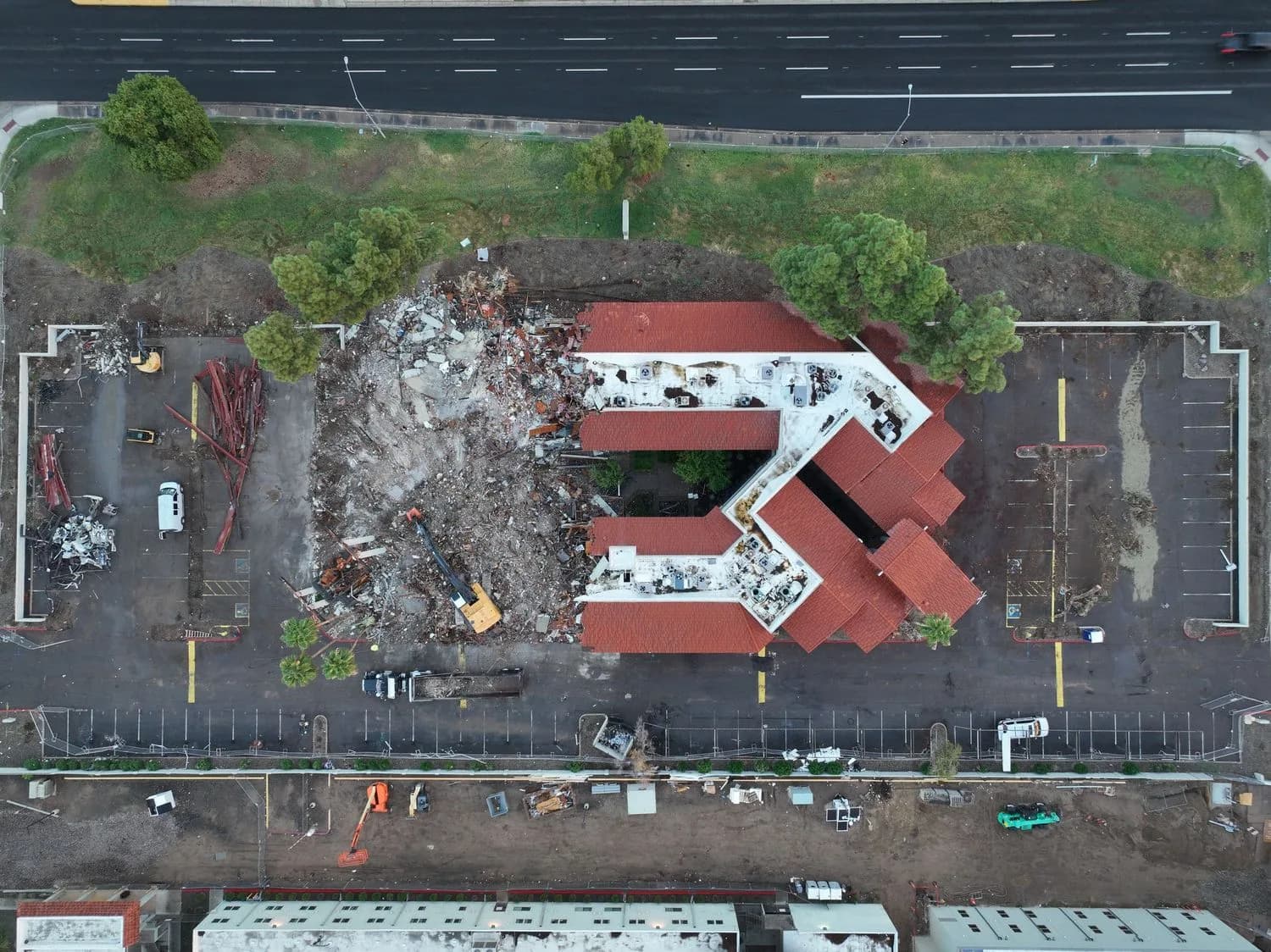 Aerial view of a partially demolished red-roofed building, rubble, excavators, and parking lots