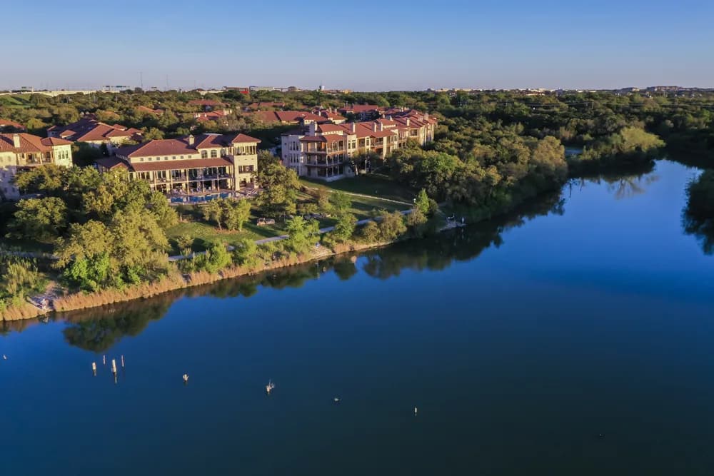 Aerial view of a riverside residential area with red-roofed buildings and green trees beside a calm blue river