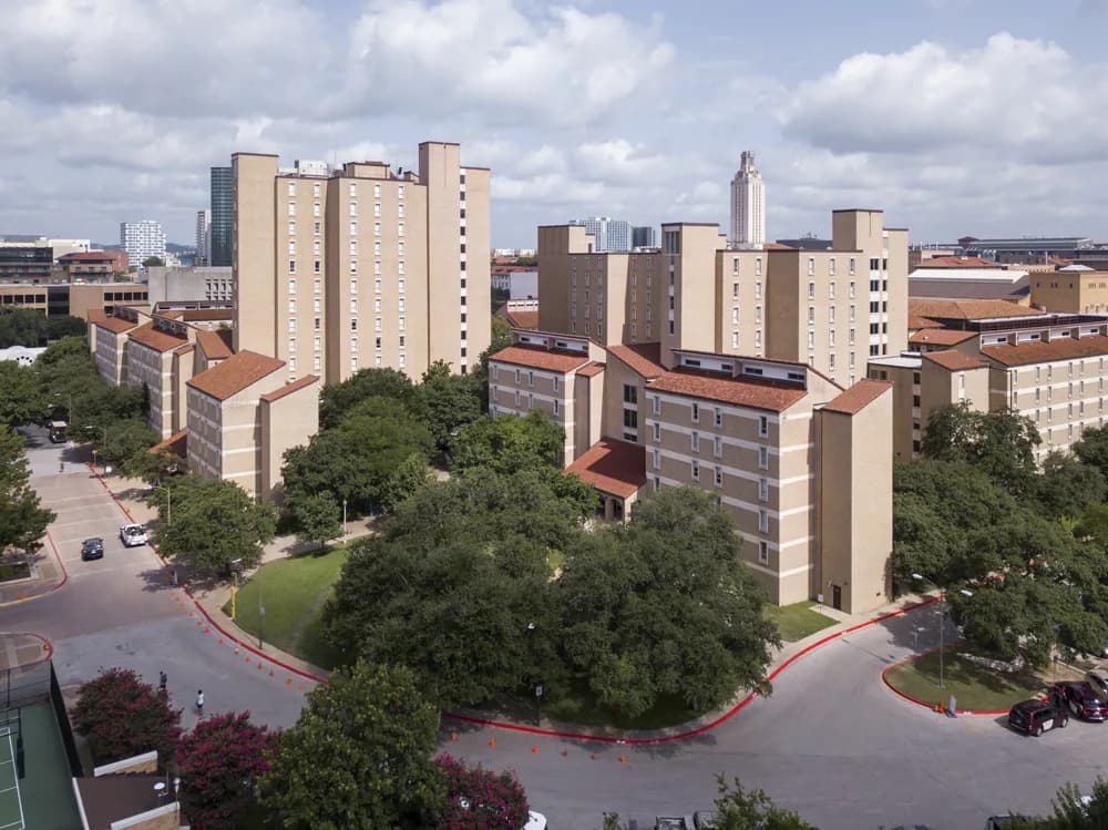 Aerial view of beige apartment buildings with red-tiled roofs, surrounded by trees and curved roads
